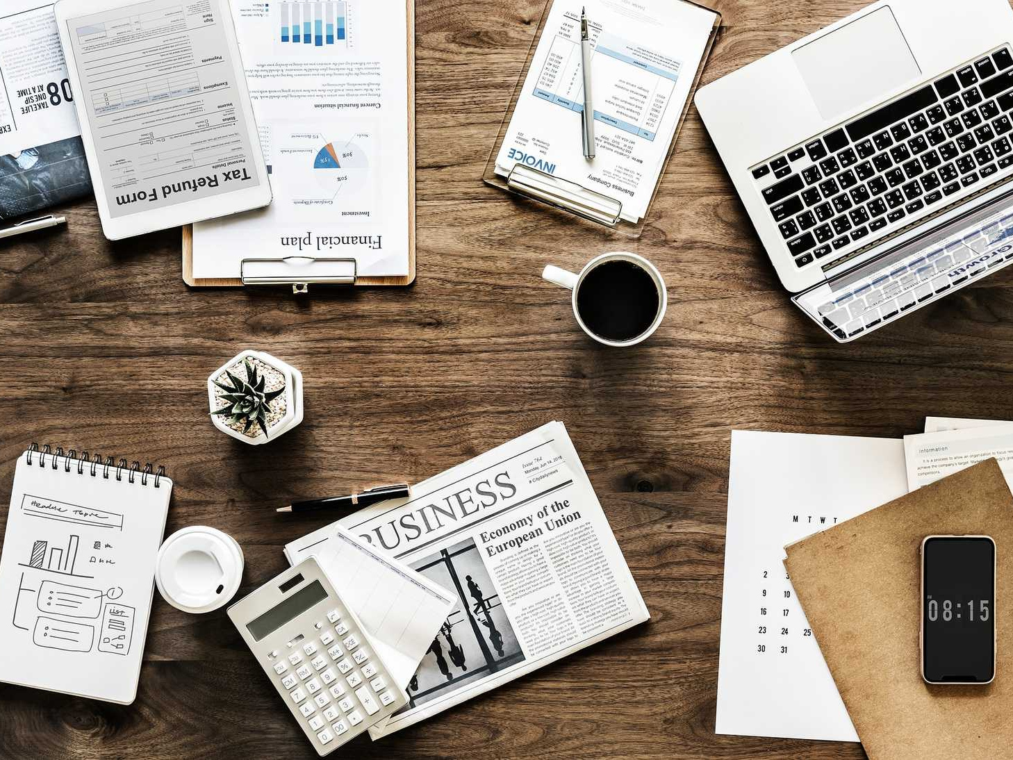 Schreibtisch mit Laptop, Smartphone, Unterlagen, Notizen und Kaffeetasse